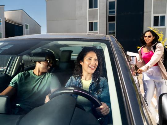 Two individuals in a stationary car as another person gets in the backseat.